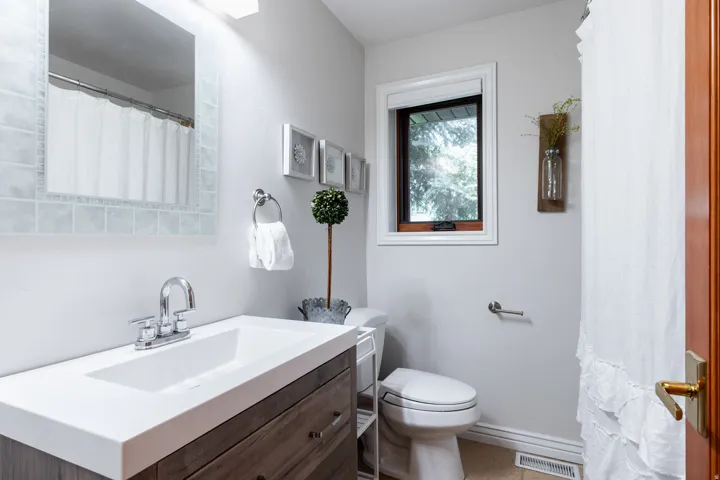 Vanity with integrated rectangular basin and chrome faucet, wood-finish cabinetry, tile-framed mirror, and a window for natural light