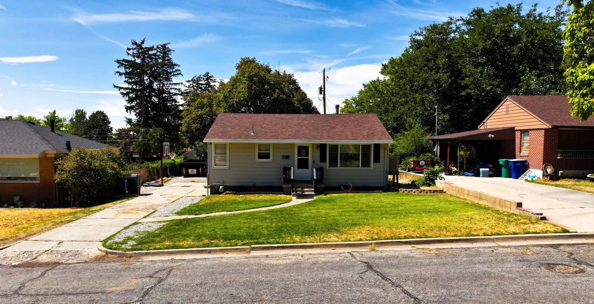 Single-story home featuring a front lawn, paved driveway, and established trees