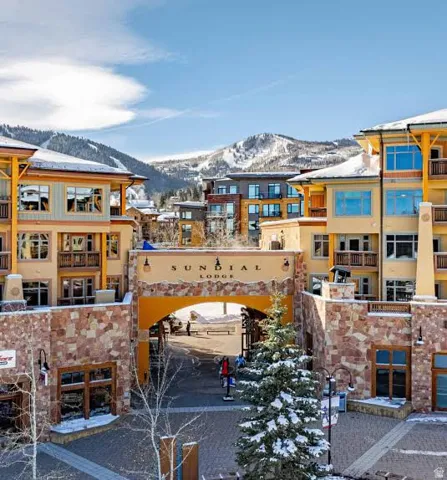 Stone-clad archway entrance to Sundial Lodge featuring multiple balconies, a paver courtyard, and mountain backdrop