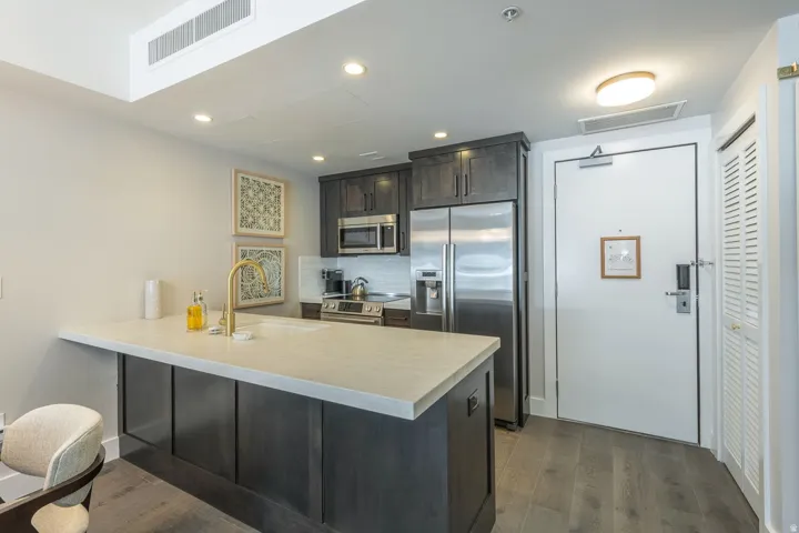 Kitchen featuring dark wood-finish cabinetry, stainless steel appliances, a light-toned countertop, and wood-finish flooring