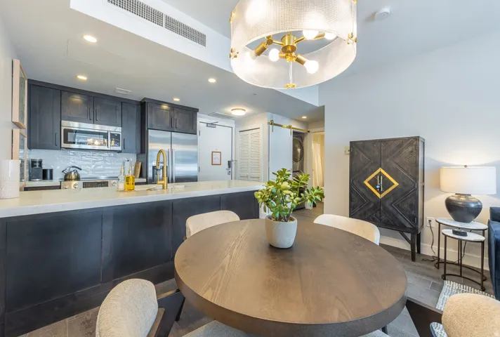 Integrated kitchen and dining area featuring dark wood-finish cabinetry, stainless steel appliances, and a white subway tile backsplash