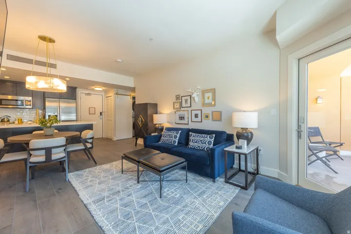 Open-concept living area with wood-finish flooring, a kitchen featuring stainless steel appliances and dark cabinetry, and a dining area with a contemporary chandelier