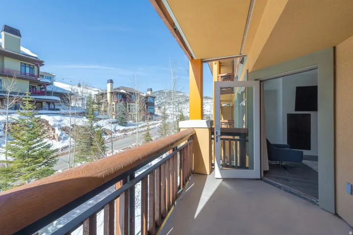 Spacious outdoor balcony with a wood-finish handrail, leading to an interior space through glass French doors