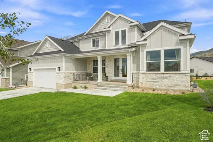 Light-toned exterior with stone veneer accents, an attached garage, and a covered porch