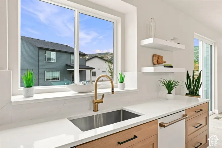 Expansive window over a stainless steel sink with a gold-finish faucet. Two White and gold Dishwashers.