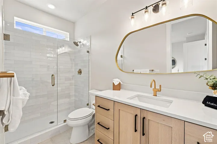 Spacious bathroom featuring a glass-enclosed shower with subway tile, light wood-finish vanity with white countertop, integrated rectangular sink, and gold-finish fixtures