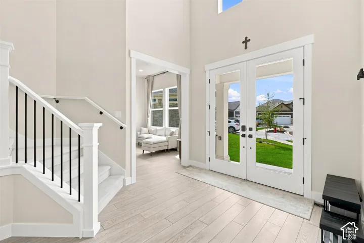 Beautiful  glass double-door entry with clear glass panels, wood like-finish flooring, staircase with black metal balusters and white risers, and two story ceilings