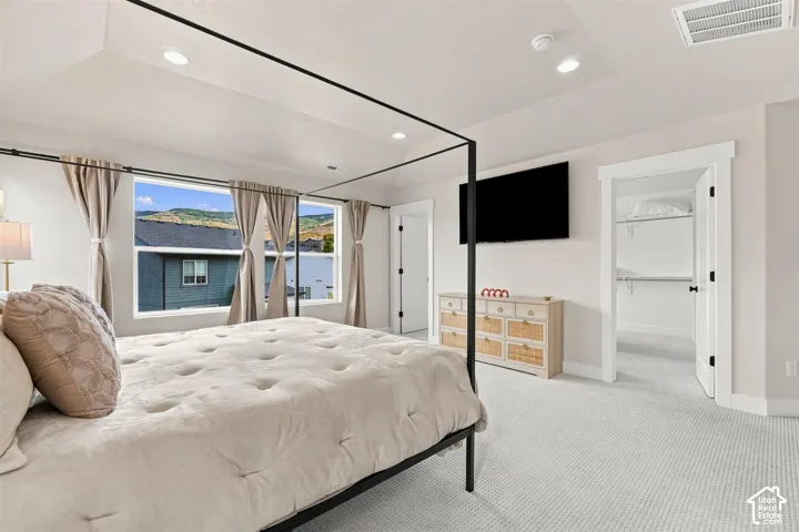 Primary Bedroom. Recessed lighting, wall-mounted television, carpet flooring, and a walk-in closet with built-in shelving