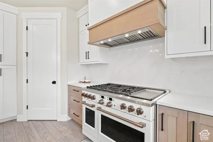 Gourmet kitchen with a professional-graded matt white and gold range, Dishwashers, refrigerator. integrated wood-finish range hood, white shaker cabinetry, white countertops, and a full-height backsplash