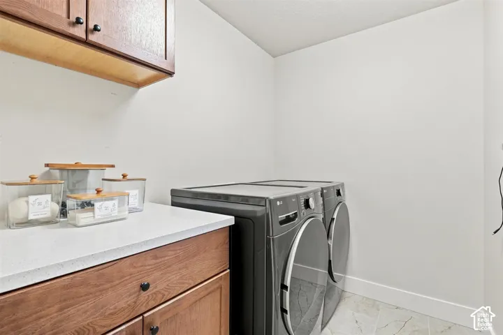 Full laundry room with washer & dryer. Wood-finish cabinetry, light-toned countertop, and tile flooring