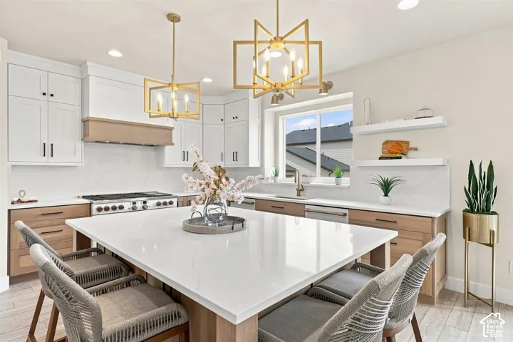 Kitchen featuring white upper cabinetry, wood-finish lower cabinetry, a large center island with a white countertop, and gold-finish pendant lighting