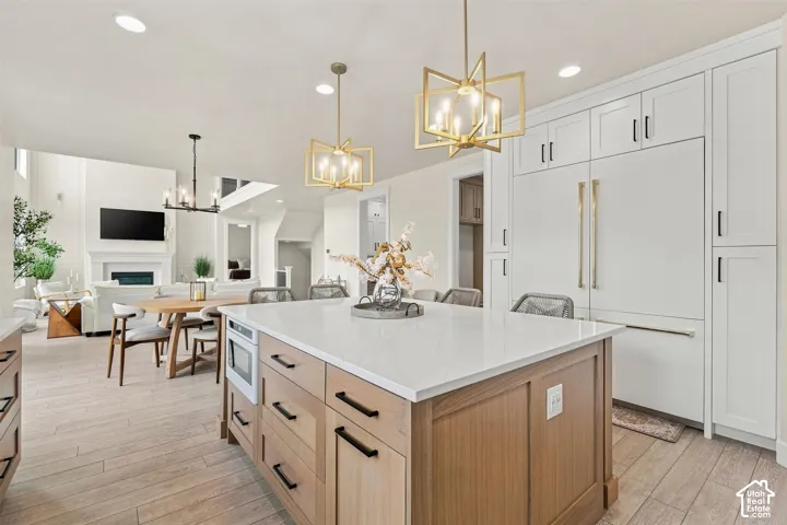White and gold double door fridge. Spacious kitchen featuring a large central island with light-toned wood-finish cabinetry, a built-in microwave, and a light-toned countertop