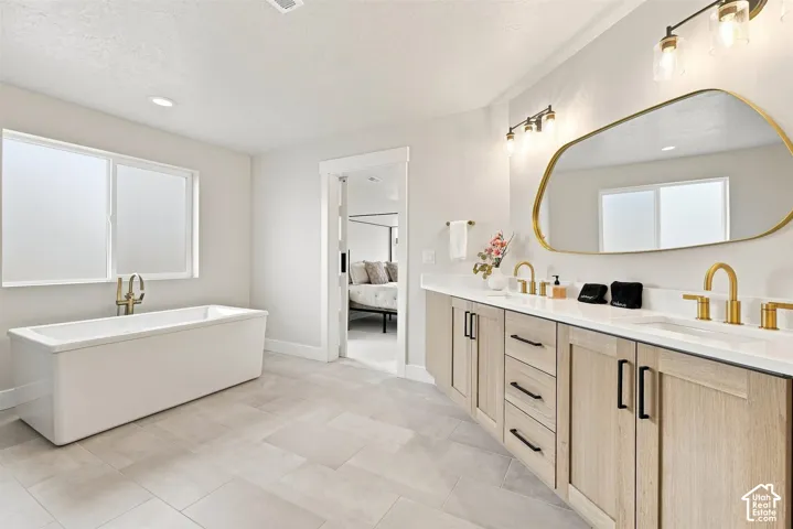 Primary bathroom. Freestanding sparkling tub with floor-mounted brass faucet, dual vanity with wood-finish cabinetry, white countertops, and brass fixtures