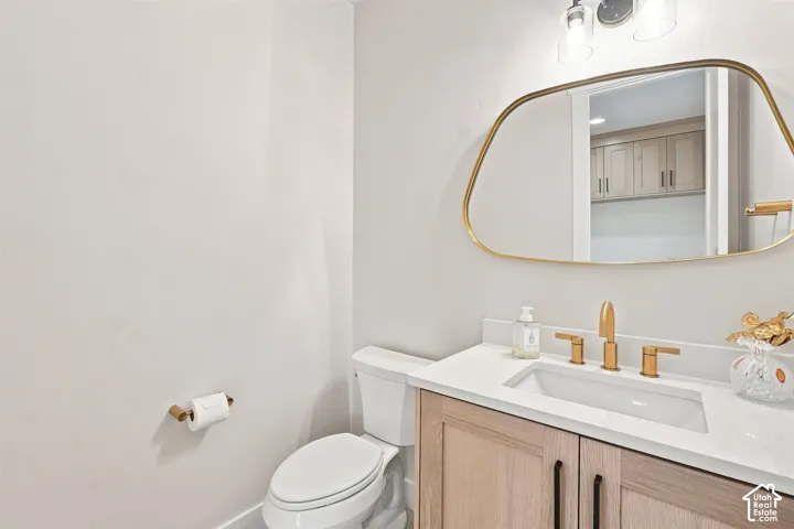 1/2 bath main floor. Modern vanity with wood-finish cabinetry, white countertop, and gold-finish fixtures. Located by mud room and kitchen