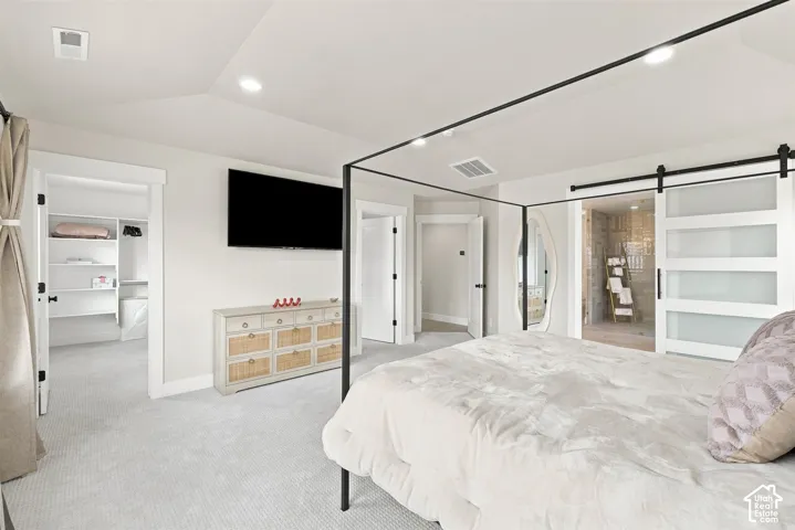 Primary Bedroom. Recessed lighting, large walk-in closet with built-in shelving, barn door access to an ensuite bathroom, and a wall-mounted television