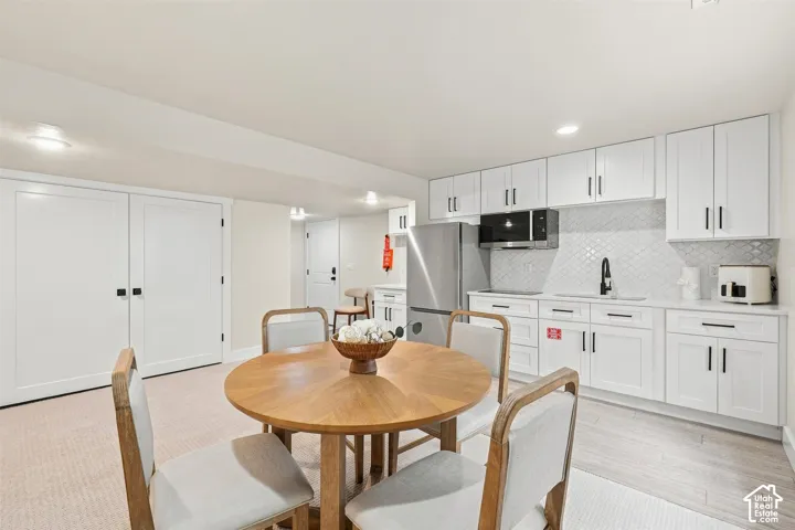 White shaker cabinetry with black hardware, stainless steel refrigerator, microwave, and a white arabesque tile backsplash. Walk out basement door.
