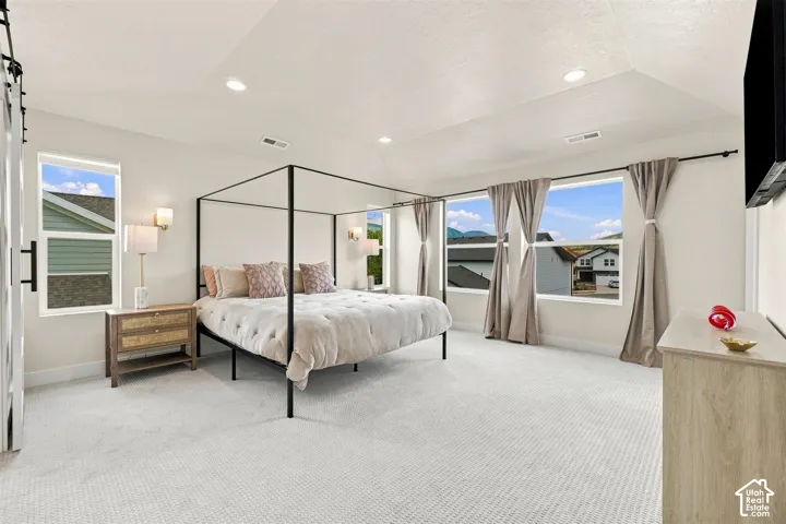 Spacious Primary Bedroom. Tray ceiling with recessed lighting, light-toned carpeting, multiple windows, and a barn door entry to bath room