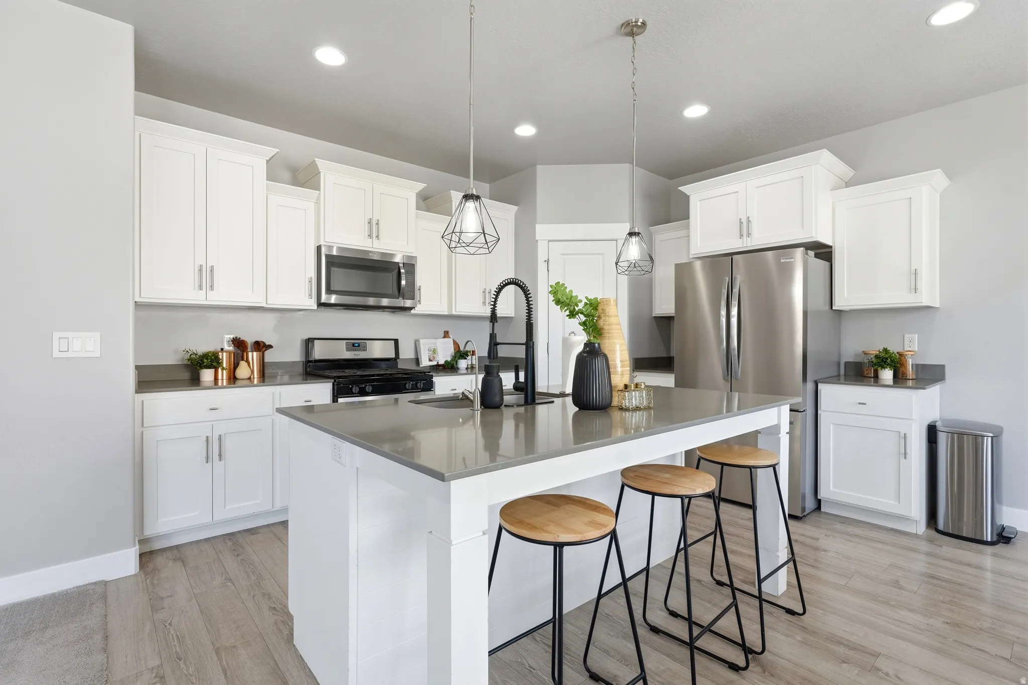Kitchen featuring white cabinetry, stainless steel appliances, a center island with countertop seating, wood-finish flooring, and recessed lighting