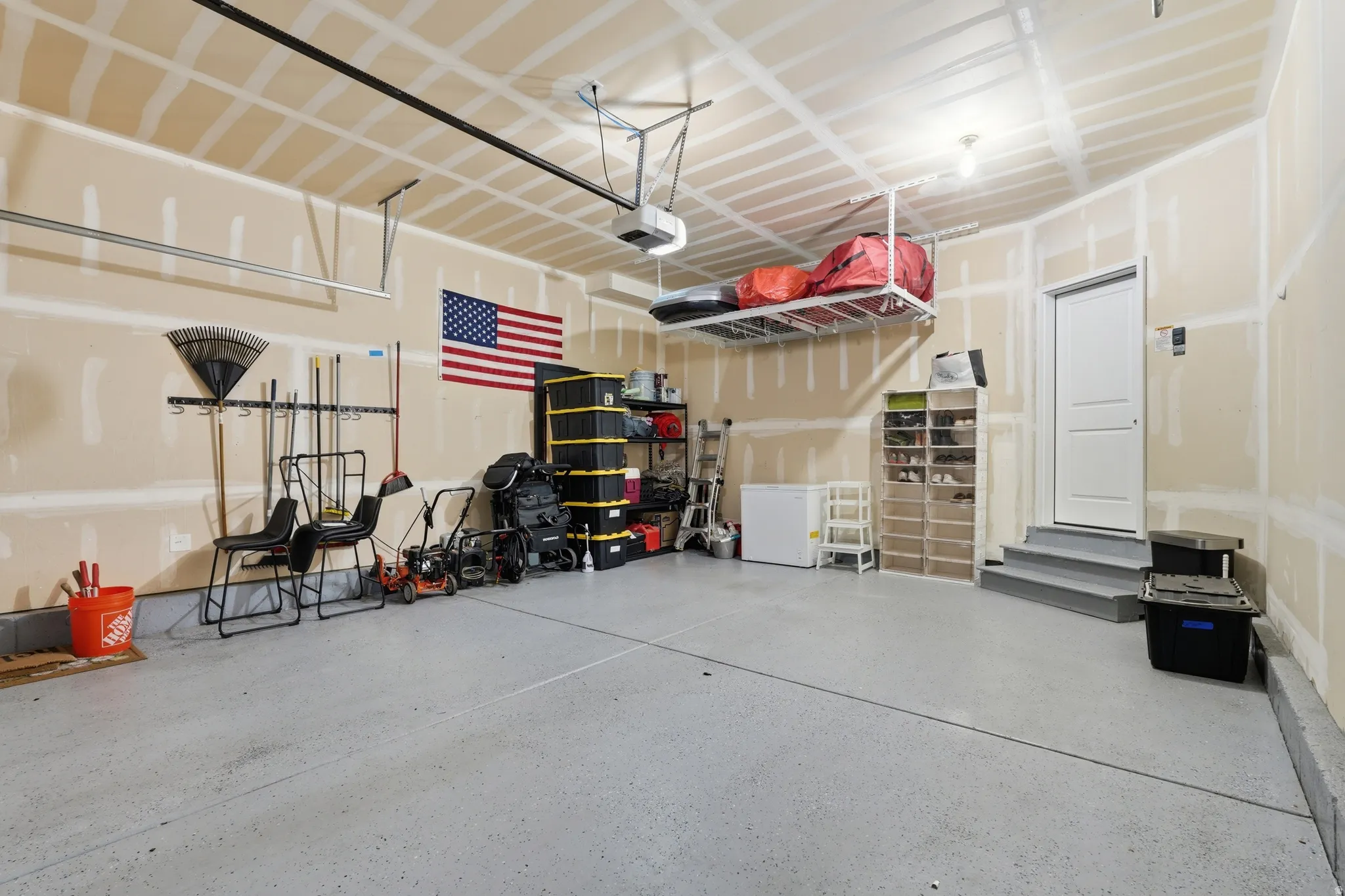 Garage featuring a gray epoxy floor coating, exposed ceiling joists, and a white entry door with gray steps