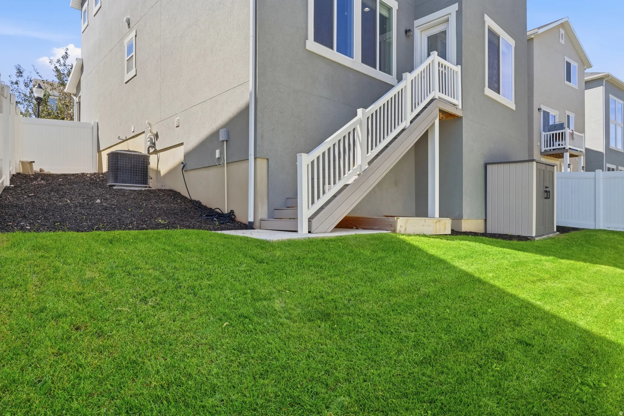 Landscaped yard featuring a white vinyl fence, exterior stairs with white railings, and a storage shed