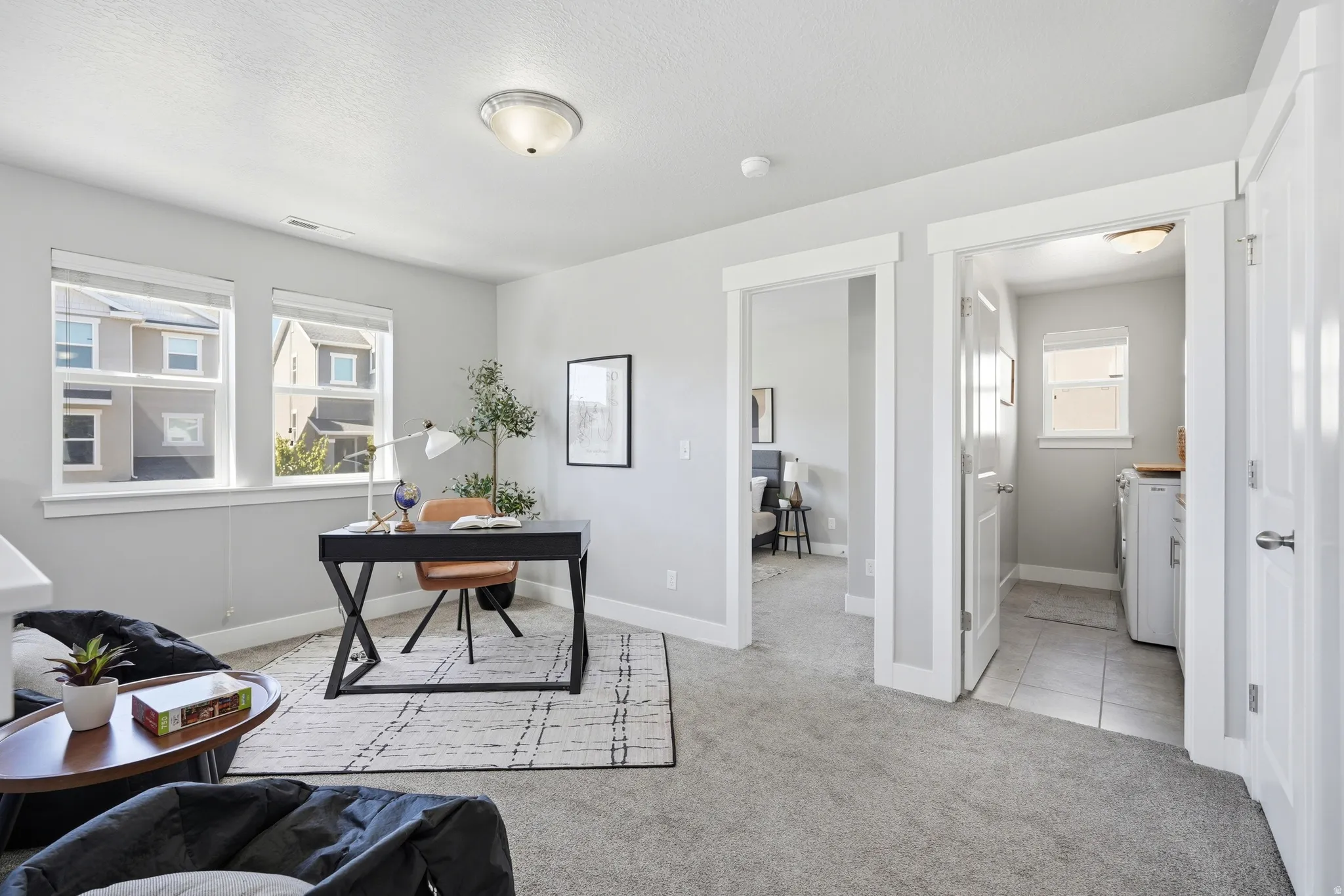 Gray wall paint throughout, two large windows with white trim, gray carpet flooring, and a laundry area with tiled flooring