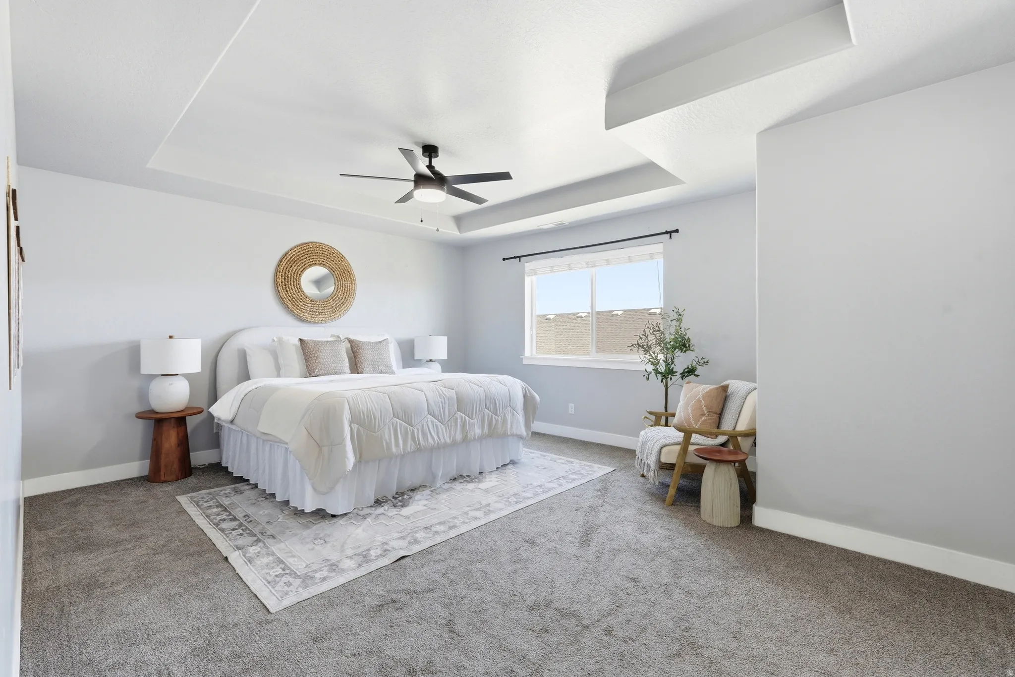 Tray ceiling, recessed lighting, ceiling fan, large window, and light gray wall paint