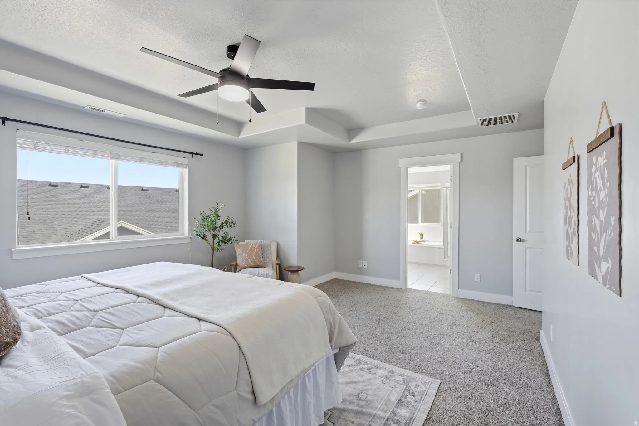 Spacious primary bedroom featuring abundant natural light from expansive windows, neutral paint finishes, carpeted flooring, ceiling fan with integrated lighting, and direct access to an ensuite bathroom