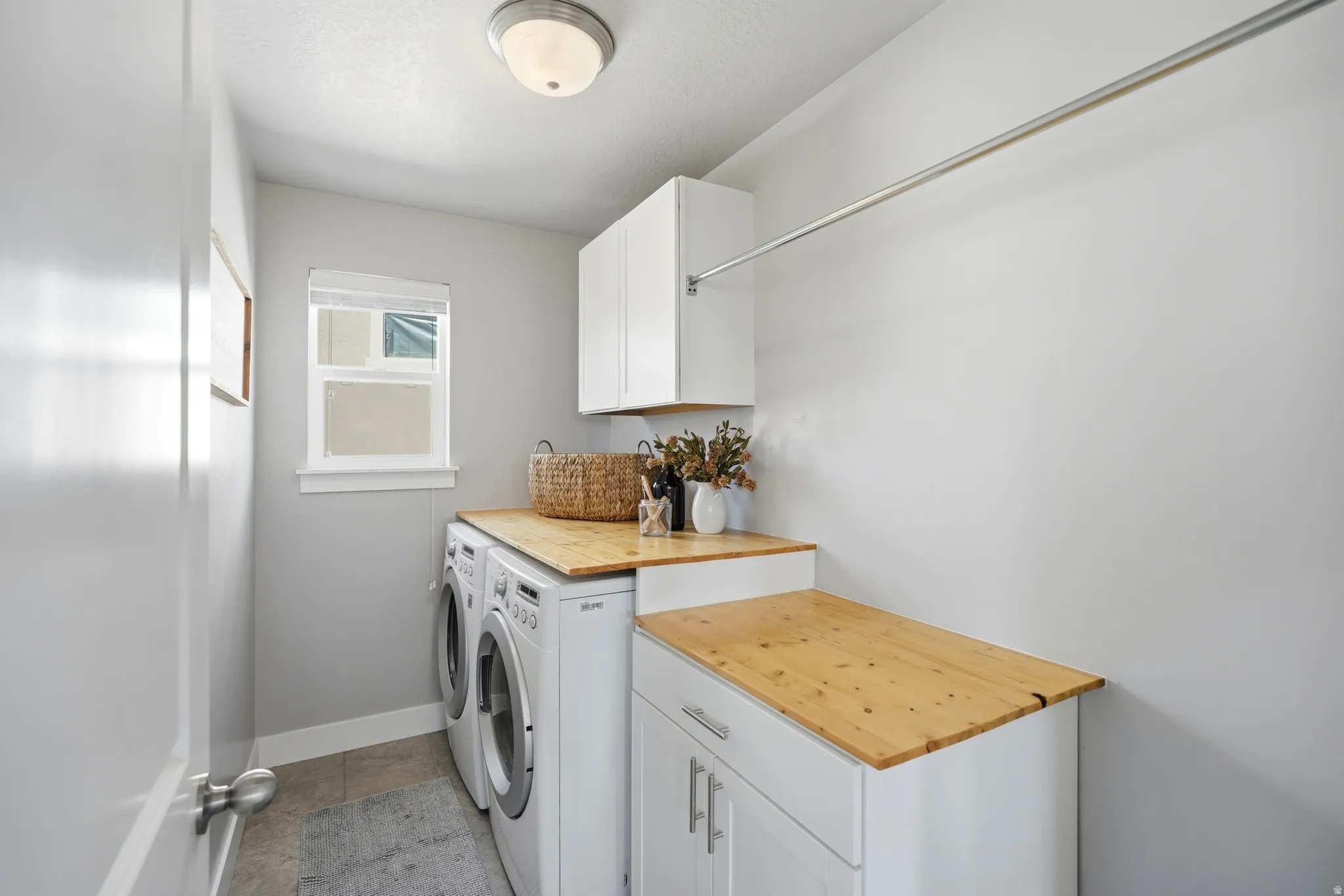 Laundry area featuring light wood-finish countertops, white cabinetry, a built-in hanging rod, and a window for natural illumination