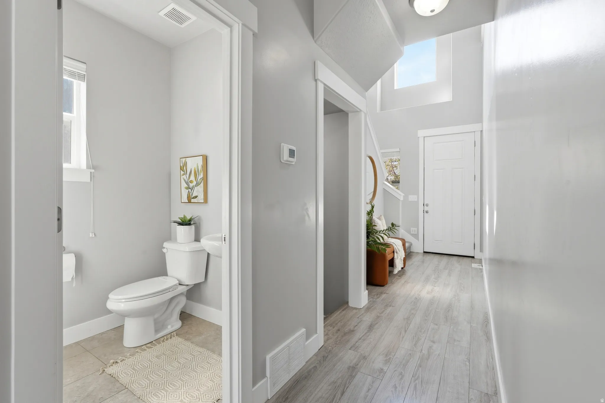 Light wood-finish flooring, a white paneled door, high ceilings, and a second-story window