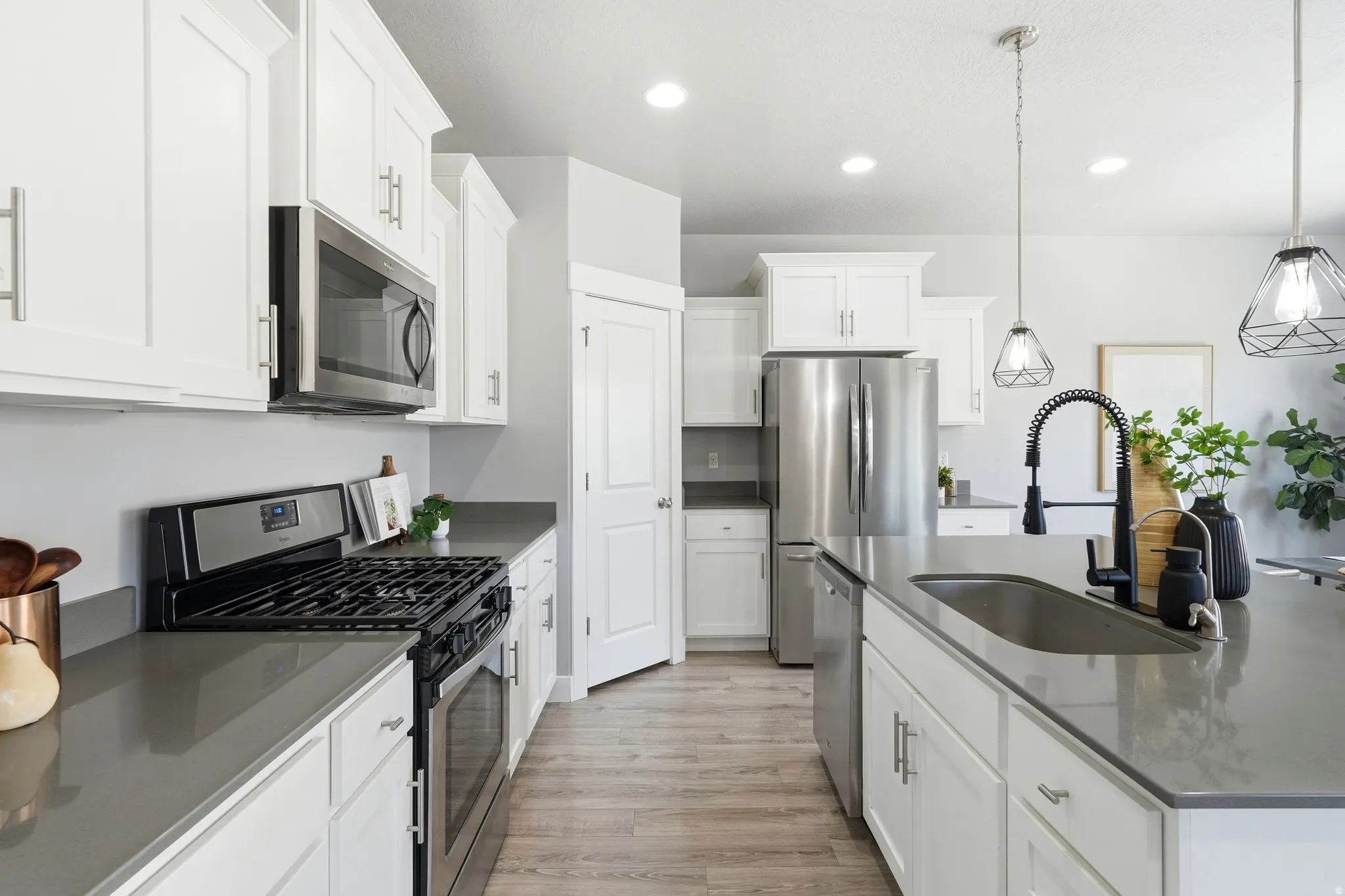 Kitchen featuring white shaker cabinetry, stainless steel appliances, dark countertops, and wood-finish flooring