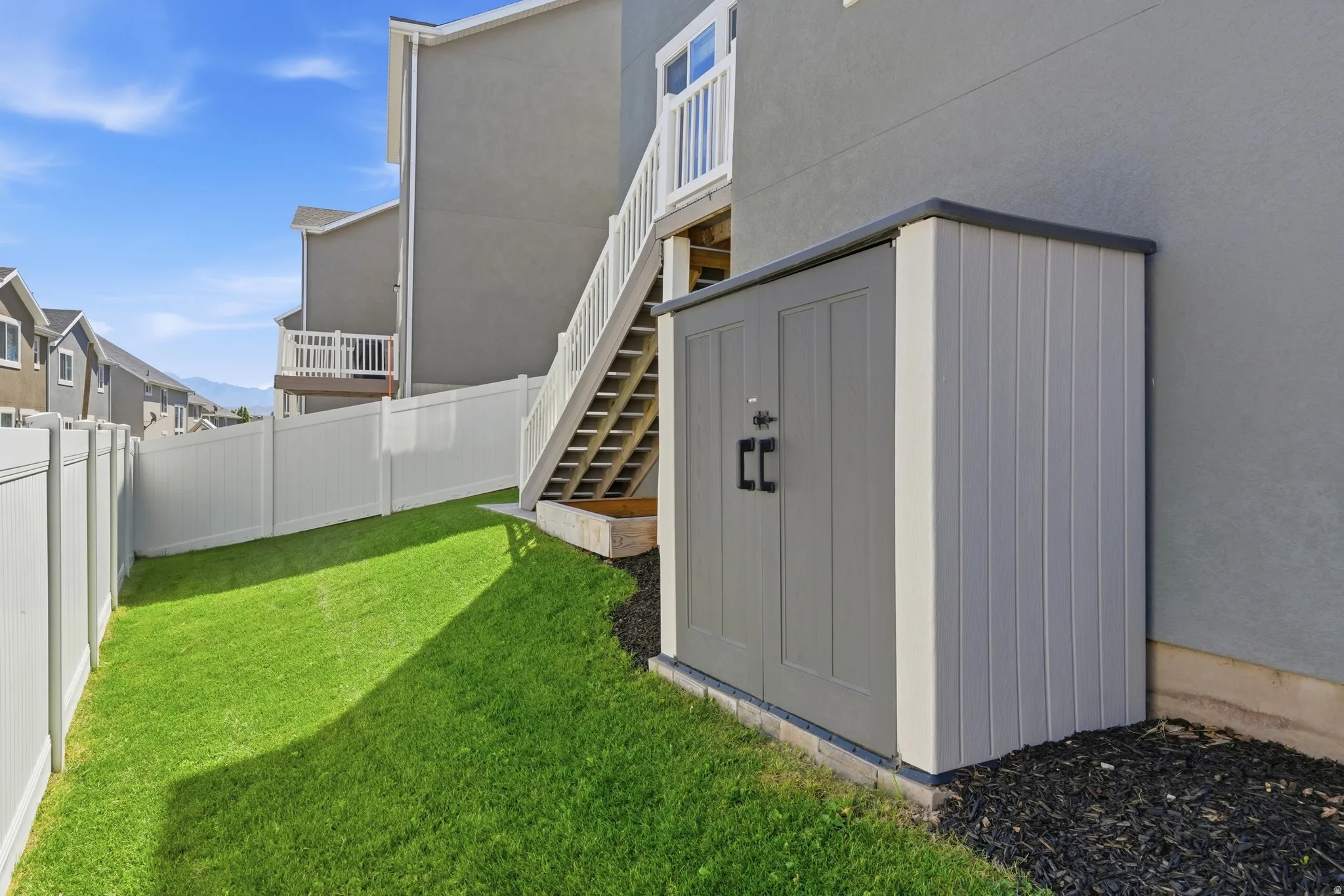 Private backyard featuring a manicured lawn, white privacy fencing, and a built-in storage shed