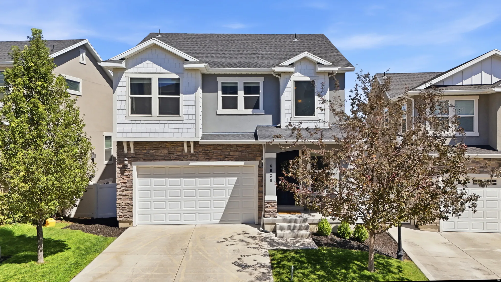 Two-story residence featuring a two-car garage, stone and shingle siding, and a concrete driveway