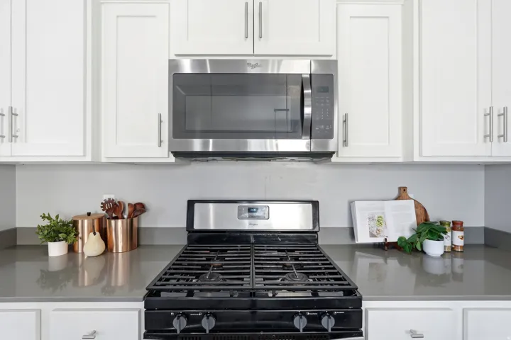 Stainless steel microwave, white shaker-style cabinetry with silver hardware, smooth grey countertops, and a black gas range
