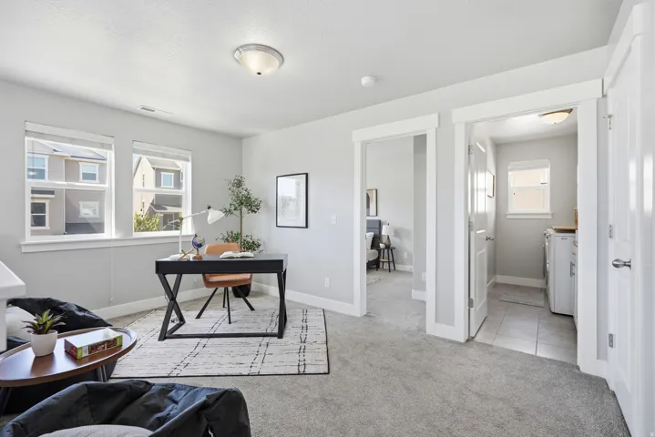 Gray wall paint throughout, two large windows with white trim, gray carpet flooring, and a laundry area with tiled flooring