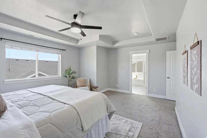 Spacious primary bedroom featuring abundant natural light from expansive windows, neutral paint finishes, carpeted flooring, ceiling fan with integrated lighting, and direct access to an ensuite bathroom