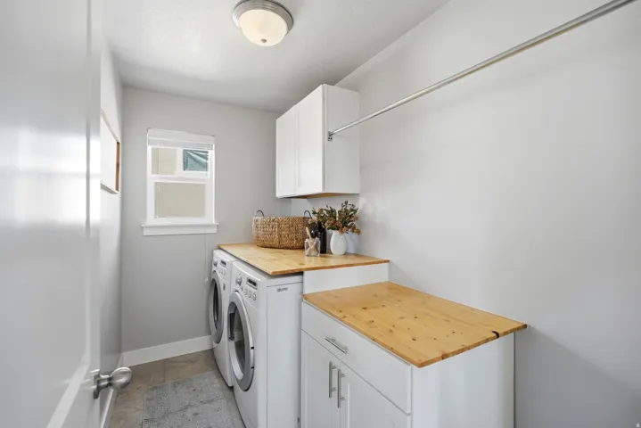 Laundry area featuring light wood-finish countertops, white cabinetry, a built-in hanging rod, and a window for natural illumination