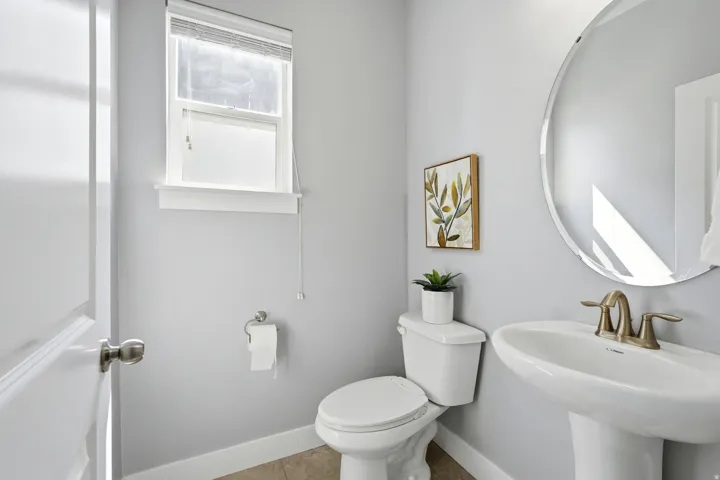 Pedestal sink with a brass-finish faucet, circular wall mirror, and a single window
