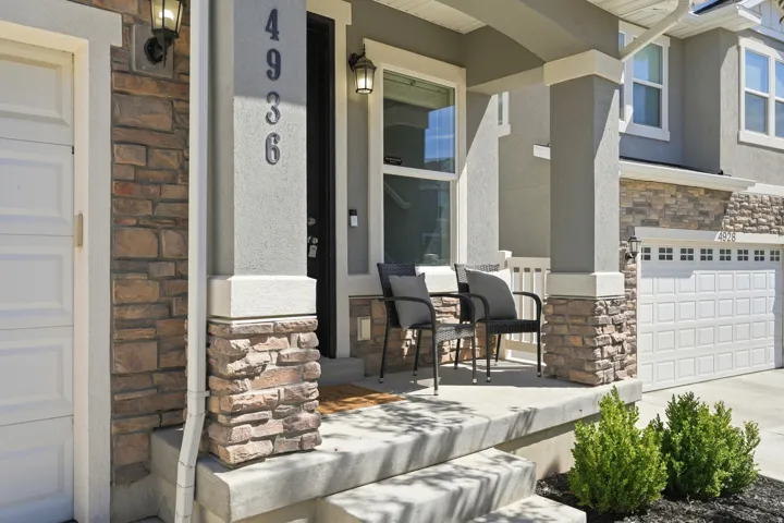 Stucco and stone facade with a covered porch, concrete steps, and integrated outdoor lighting
