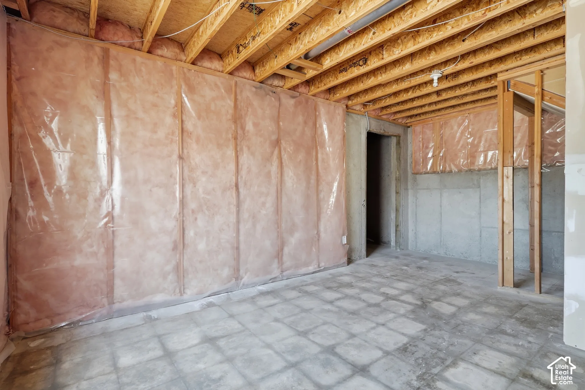 Unfinished basement with concrete flooring, exposed wooden ceiling joists, and insulated walls