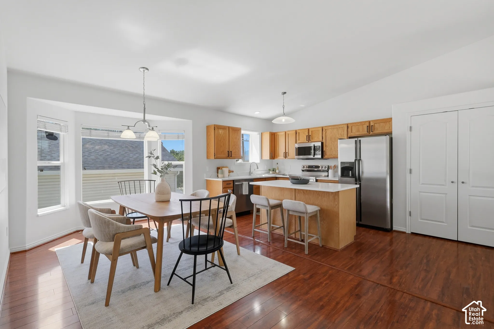 Hardwood flooring, bay windows, kitchen island with seating, stainless steel appliances, and wood cabinetry