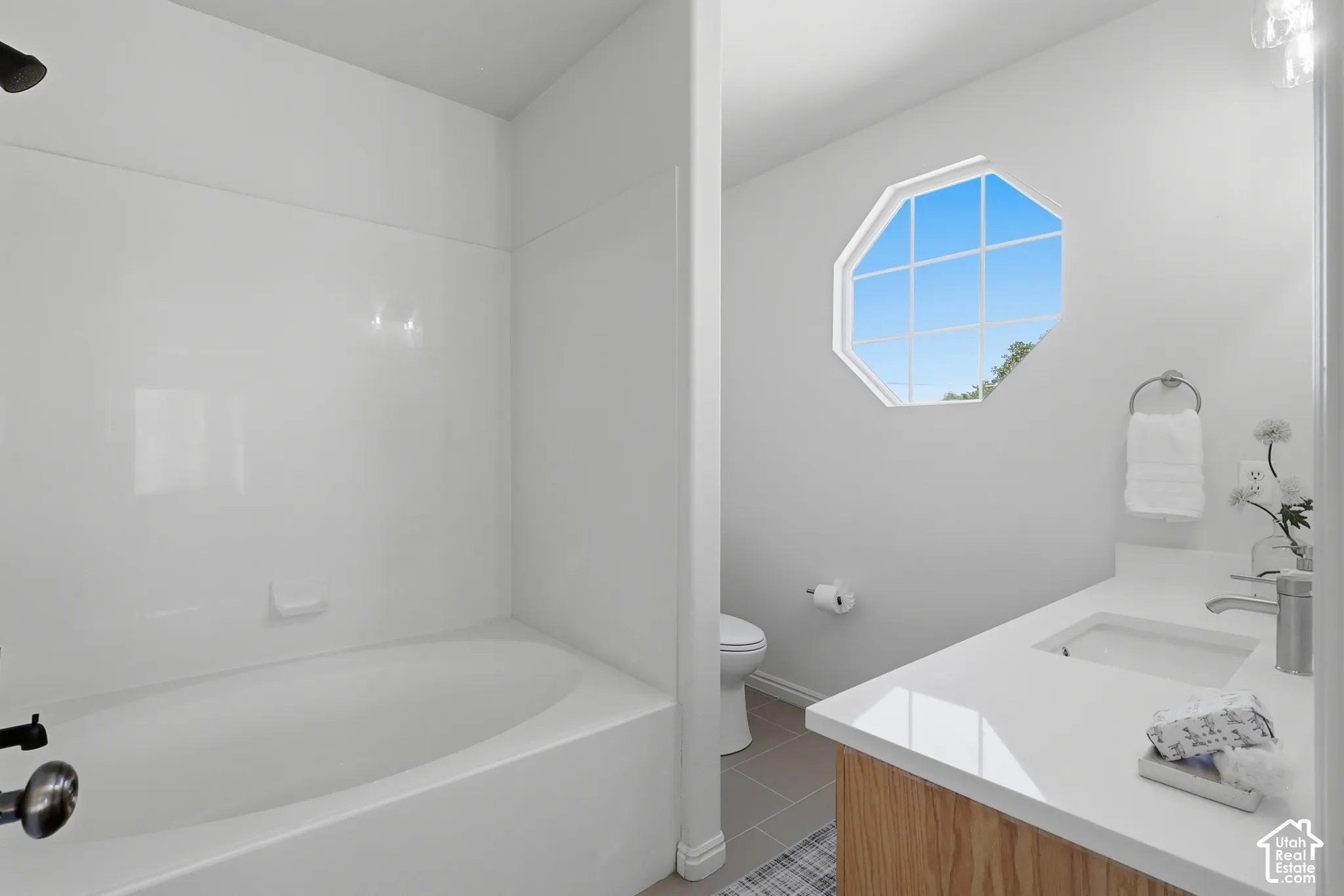Bathroom featuring a built-in bathtub with shower, wood-finish vanity with an integrated sink, white countertop, and an octagonal window