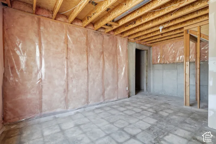 Unfinished basement with concrete flooring, exposed wooden ceiling joists, and insulated walls