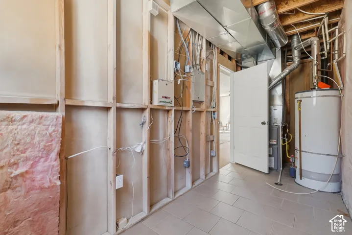 Tiled flooring, exposed wall studs, visible insulation, electrical wiring, and a water heater