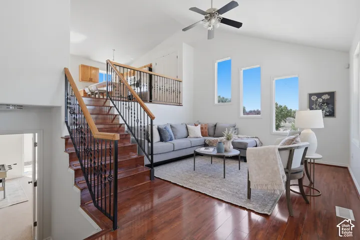 Vaulted ceiling with a ceiling fan, abundant natural light from multiple windows, rich wood-finish flooring, and a staircase featuring wrought iron balusters with wood handrails