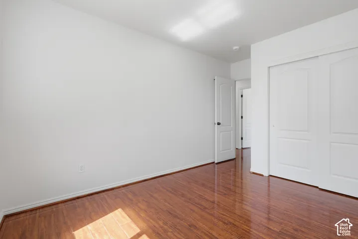 Wood-finish flooring with white baseboards, a white door with black hardware, and white sliding closet doors