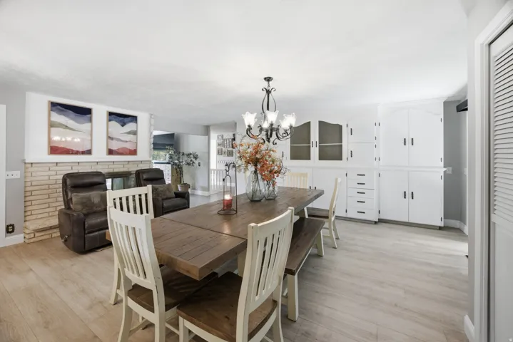Light wood-finish flooring extending throughout, a stone-clad fireplace, and a decorative chandelier
