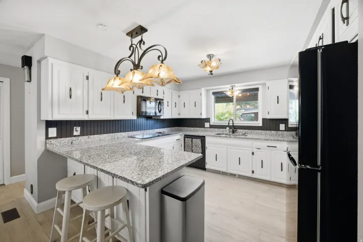 Kitchen featuring white cabinetry, granite countertops, black appliances, wood-finish flooring, and a peninsula with seating