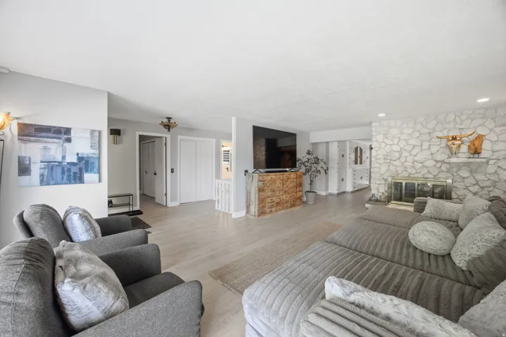 Expansive living area featuring light wood-finish flooring, a stone-clad fireplace, and recessed lighting