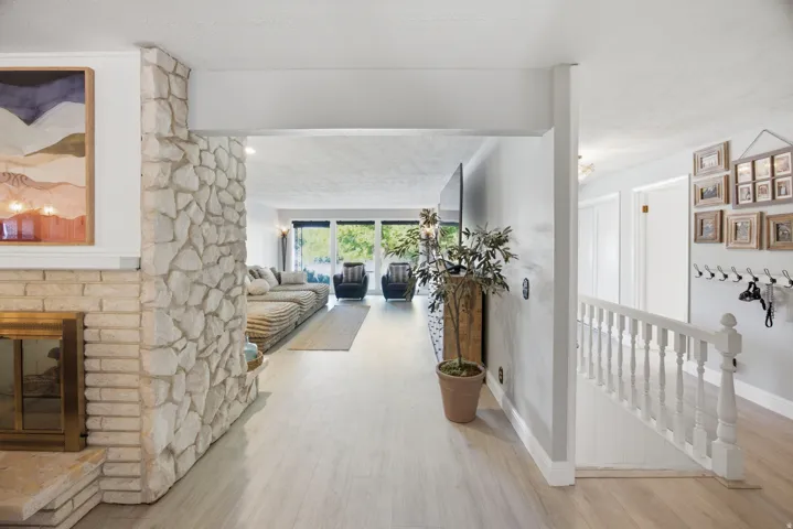 Stone-clad fireplace with a brass firebox, light wood-finish flooring, and a white baluster railing