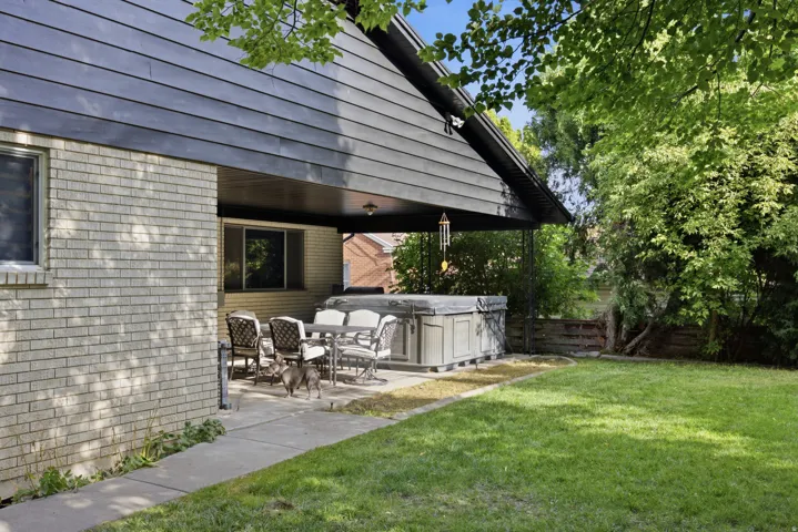 Expansive backyard with a manicured lawn, covered patio, and attached spa